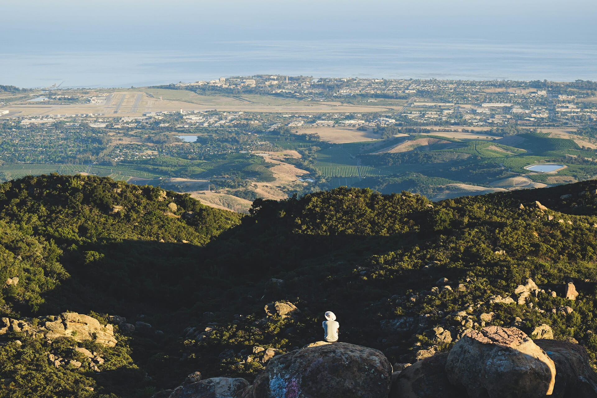 Hiker overlooking a valley and cityscape from hilltop.